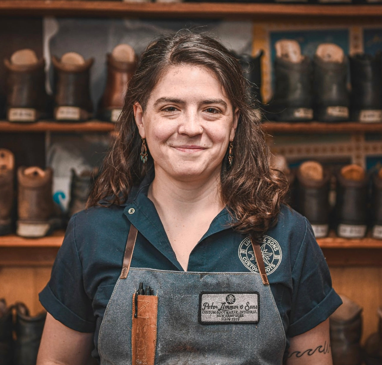 Woman wearing an apron in a shoe store with shelves of boots behind her